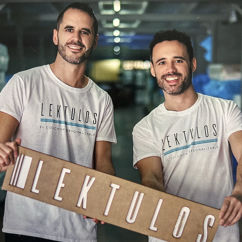 Manel y Albert, fundadores de Lektulos, con camisetas y el cartel de Lektulos